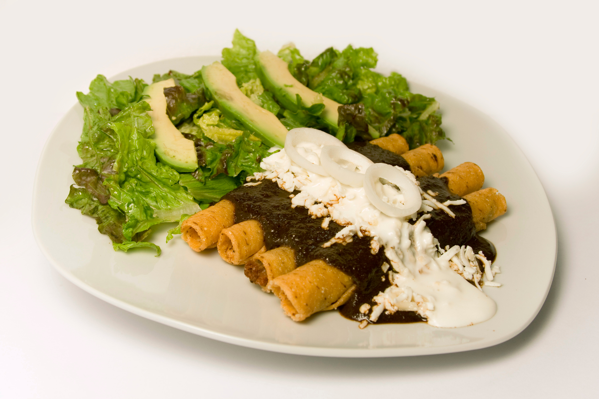 Golden flautas topped with mole, crema and cheese